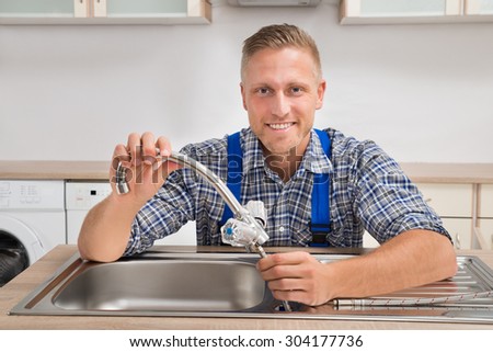 Young Male Plumber Fixing Faucet In Sink Of Kitchen