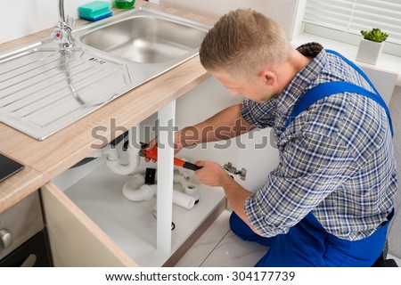 Male Plumber Fixing Sink Pipe With Adjustable Wrench In Kitchen