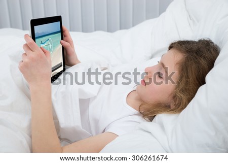 Girl Resting On Bed While Watching Video On Digital Tablet In Bedroom
