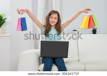 Happy Girl Holding Small Multi-colored Shopping Bags With Laptop On Sofa