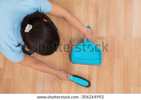 Young Woman Brooming Wooden Floor With Broom And Dustpan