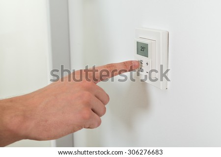 Close-up Of Person Hands Adjusting Room Temperature On A Digital Thermostat