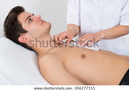 Close-up Of Beauty Therapist Waxing Young Man\'s Chest Lying On Bed