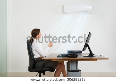 Young Businesswoman Sitting On Chair Using Air Conditioner In Office