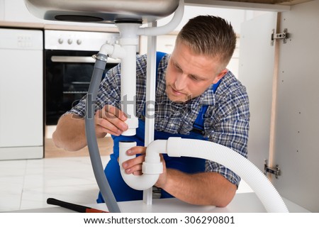 Young Plumber Repairing Pipe Of Sink In Kitchen