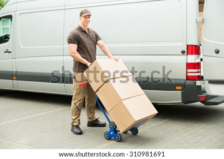 Young Delivery Man Holding Trolley With Cardboard Boxes