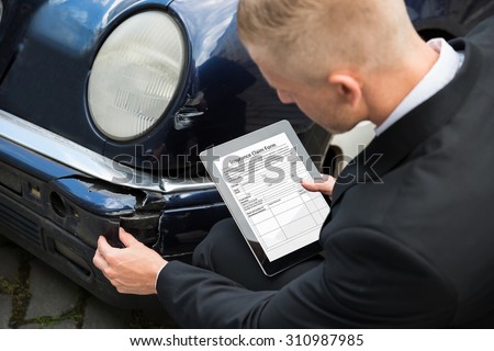 Insurance Agent Inspecting Damaged Car With Insurance Claim Form On Digital Tablet