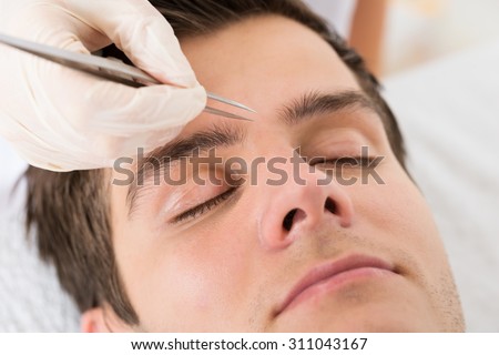 Close-up Of Beautician Hands Plucking Handsome Man Eyebrows With Tweezers