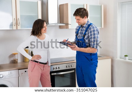 Repairman Writing On Clipboard While Beautiful Woman Standing In Kitchen