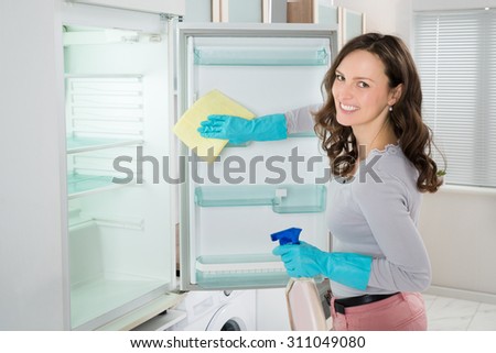 Young Woman Cleaning Refrigerator With Rag At Home
