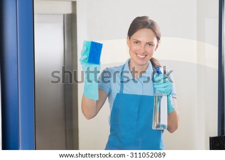 Young Happy Female Janitor Cleaning Glass With Detergent Spray Bottle And Sponge