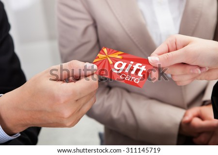 Close-up Of Businessperson Hands Giving Gift Card To Other Businessperson