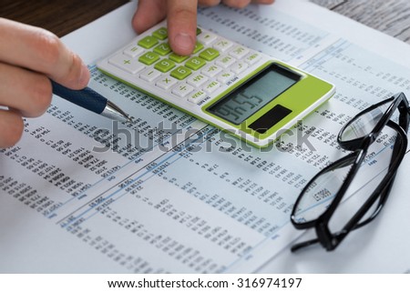 Close-up Of Person Hands Analyzing Accounting Document With Calculator
