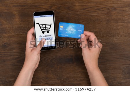 Person Hands Shopping Online With Credit Card On Mobile Phone At Wooden Desk