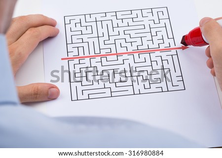 Close-up Of Person Drawing Straight Red Line Over Maze With Red Marker