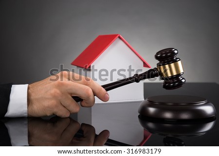 Close-up Of Judge With House Model Hitting Gavel At Desk