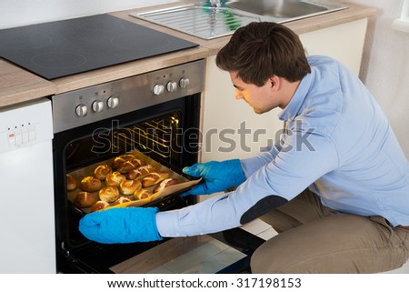 Young Man Taking Baking Tray With Baked Bread From Oven In Kitchen