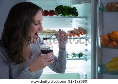Young Woman Eating In Front Of Fridge In Kitchen