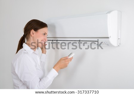 Happy Businesswoman Operating Air Conditioner Mounted On White Wall In Office