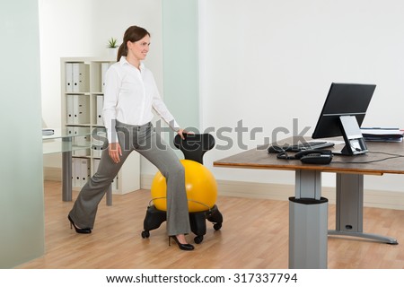 Young Happy Businesswoman Exercising With Pilates Ball On Chair In Office
