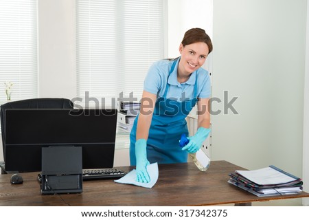 Young Happy Worker Cleaning Desk With Rag In Office