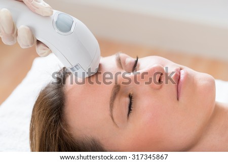 Close-up Of Beautician Giving Laser Epilation Treatment To Young Woman Face