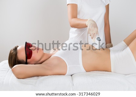 Young Woman Lying On Bed Receiving Epilation Laser Treatment On Tummy