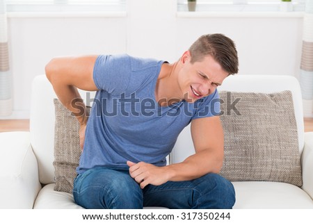 Young Man On Sofa Suffering From Backpain At Home