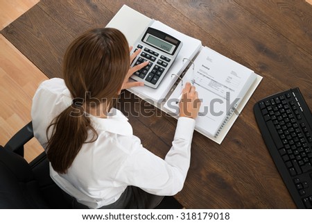 Young Businesswoman With Invoice And Calculator At Wooden Desk