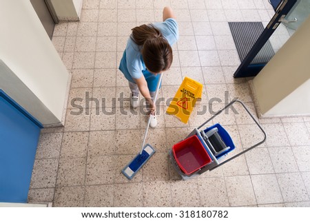 Female Janitor Mopping Floor With Cleaning Equipments And Wet Floor Sign On Floor