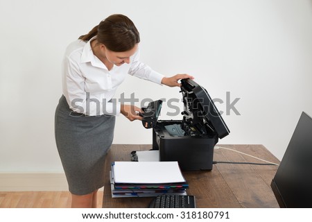 Young Businesswoman At Desk Putting Laser Toner Cartridge In Printer
