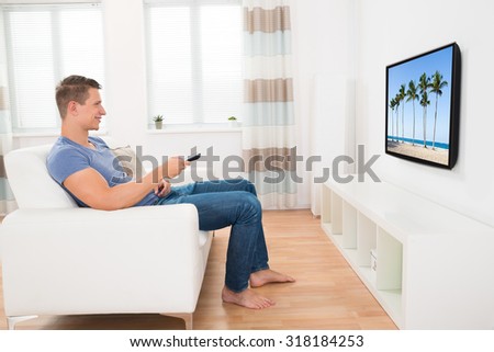 Young Man Sitting On Sofa Watching Television At Home