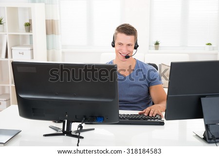 Happy Man Talking With Headset On Computer At Desk