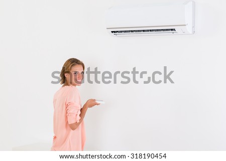 Young Woman Operating Air Conditioner With Remote Control