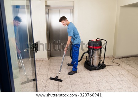 Happy Male Worker Cleaning Floor With Vacuum Cleaner Appliance