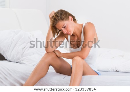 Depressed Young Woman In Tanktop Sitting On Bed
