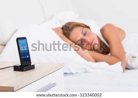Young Woman Sleeping In Bed With Alarm On Mobile Phone Display