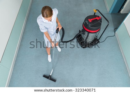 High Angle View Of Female Worker Cleaning Floor With Vacuum Cleaner