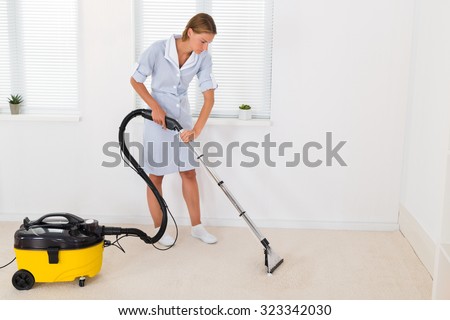 Young Female Maid Cleaning Floor With Vacuum Cleaner