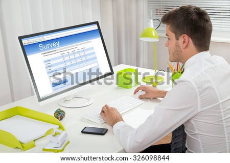 Young Businessman Filling Online Survey Form On Computer At Desk