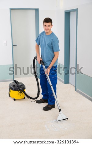 Young Male Cleaner In Uniform Vacuuming Floor