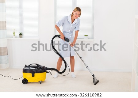 Young Female Maid In Uniform Vacuuming Floor