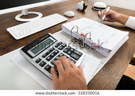 Close-up Of Businessman Checking Invoice With Calculator At Desk