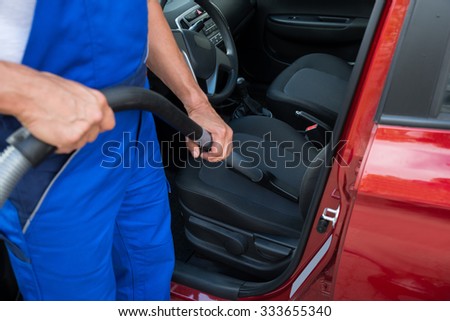 Low section of mature worker vacuuming car with vacuum cleaner