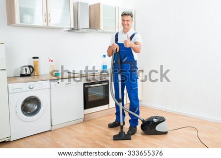 Full length portrait of male janitor cleaning floor with vacuum cleaner in kitchen
