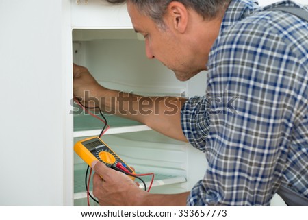 Cropped image of male repairman checking fridge with digital multimeter at home