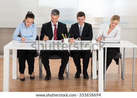 Happy Businesspeople Writing On Clipboard At Desk