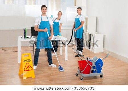 Cleaners Team In Uniform Cleaning Wooden Floor In Office