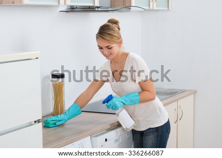 Young woman cleaning kitchen counter with sponge at home
