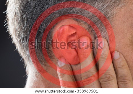 Closeup of man covering ear with hand on gray background